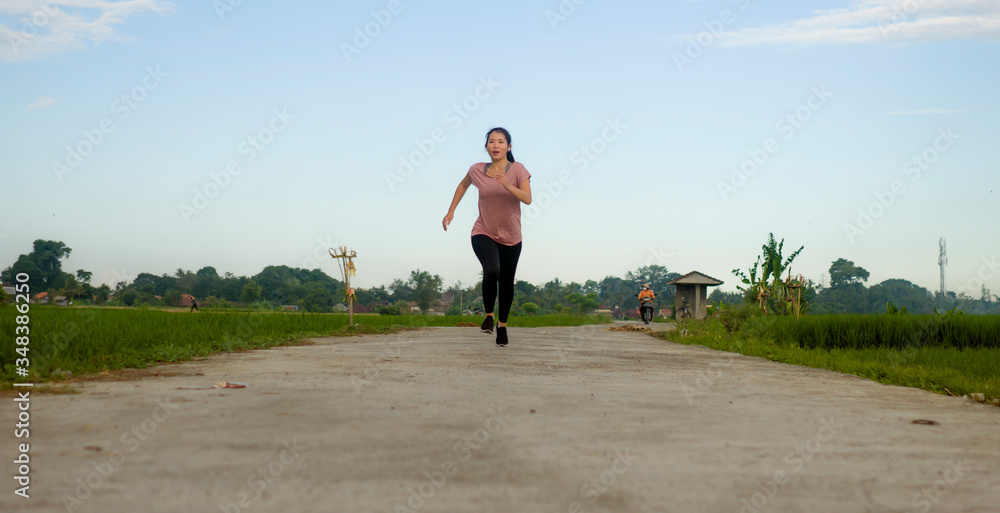outdoors jogging - young happy and dedicated Asian Korean woman running workout at beautiful ccountryside road under a blue sky on enjoying fitness and cardio