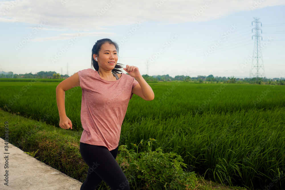 outdoors jogging - young happy and dedicated Asian Chinese woman running workout at beautiful ccountryside road under a blue sky on enjoying fitness and cardio