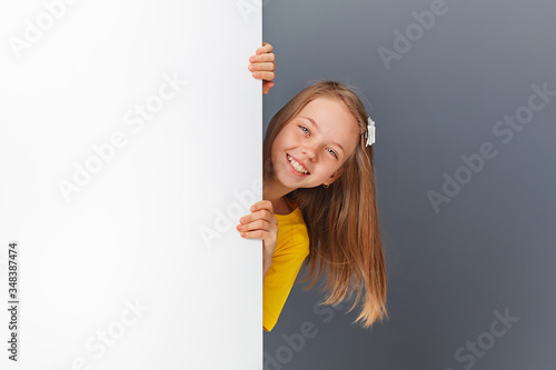 A cheerful little girl looks over a white wall or signboard highlighted on a white background.