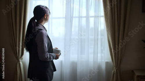 Side view of sad businesswoman holding cup and standing before window indoors