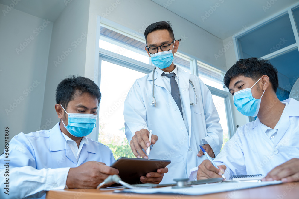 Doctor wearing protective mask to Protect Against Covid-19 meeting at hospital,Digital tablet laptop computer smart phone using,Medical technology network team meeting concept. Doctor wearing protective mask to Protect Against Covid-19 meeting at hospital,Digital tablet laptop computer smart phone using,Medical technology network team meeting concept.