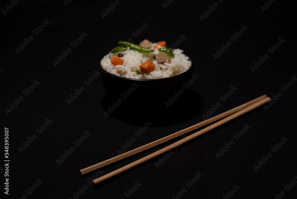 A bowl of rice with vegetables and soya chunks along with chopsticks in a black copy space background. Food photography. A bowl of rice with vegetables and soya chunks along with chopsticks in a black copy space background. Food photography.