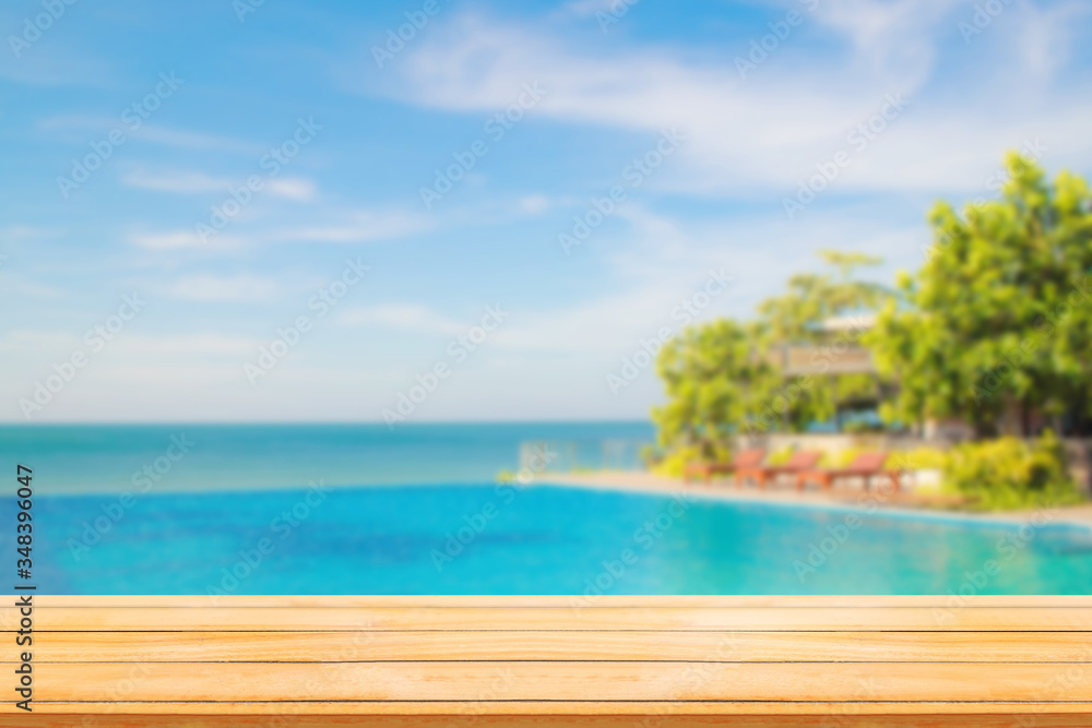 Summer Vacation Concept : Wooden table with Blurry image of Tropical beautiful seascape view of pool and blue sky in background.