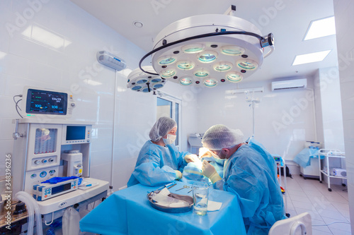 Photo of a vital signs monitor and medical equipment next to two surgeons performing surgery in the operating room