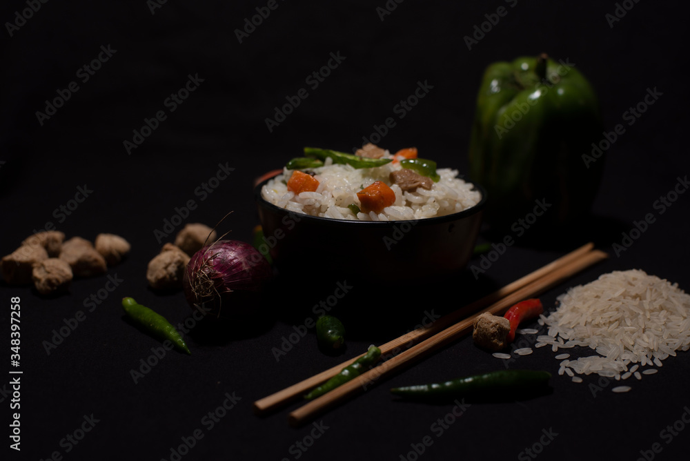 A bowl of a steamed rice and vegetables decorated with veggies, grains, chopsticks and spoon in a black copy space background. Food photography. A bowl of a steamed rice and vegetables decorated with veggies, grains, chopsticks and spoon in a black copy space background. Food photography.