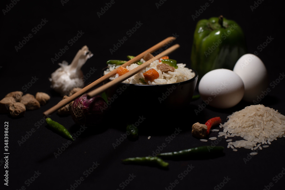 A bowl of a steamed rice and vegetables decorated with veggies, eggs, grains, chopsticks and spoon in a black copy space background. Food photography. A bowl of a steamed rice and vegetables decorated with veggies, eggs, grains, chopsticks and spoon in a black copy space background. Food photography.