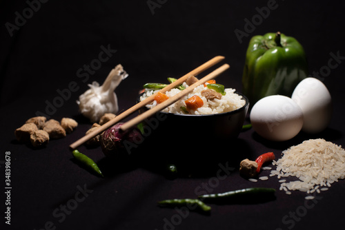 A bowl of a steamed rice and vegetables decorated with veggies, eggs, grains, chopsticks and spoon in a black copy space background. Food photography.