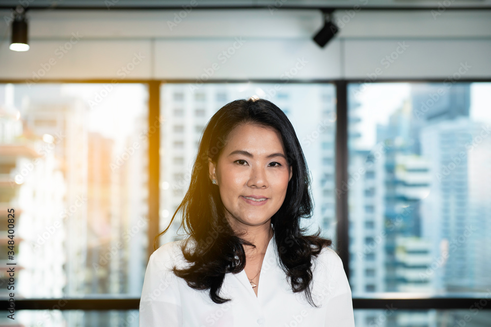Portrait of a smiling adult Asian businesswoman and dark hair in shirt posing against a building background.Indoor beautiful happy woman against city scape background. Portrait of a smiling adult Asian businesswoman and dark hair in shirt posing against a building background.Indoor beautiful happy woman against city scape background.