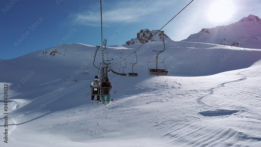 Two skiers riding a chair lift to the summit of Silvretta Montafon Ski Arena Austria, slow motion Two skiers riding a chair lift to the summit of Silvretta Montafon Ski Arena Austria, slow motion