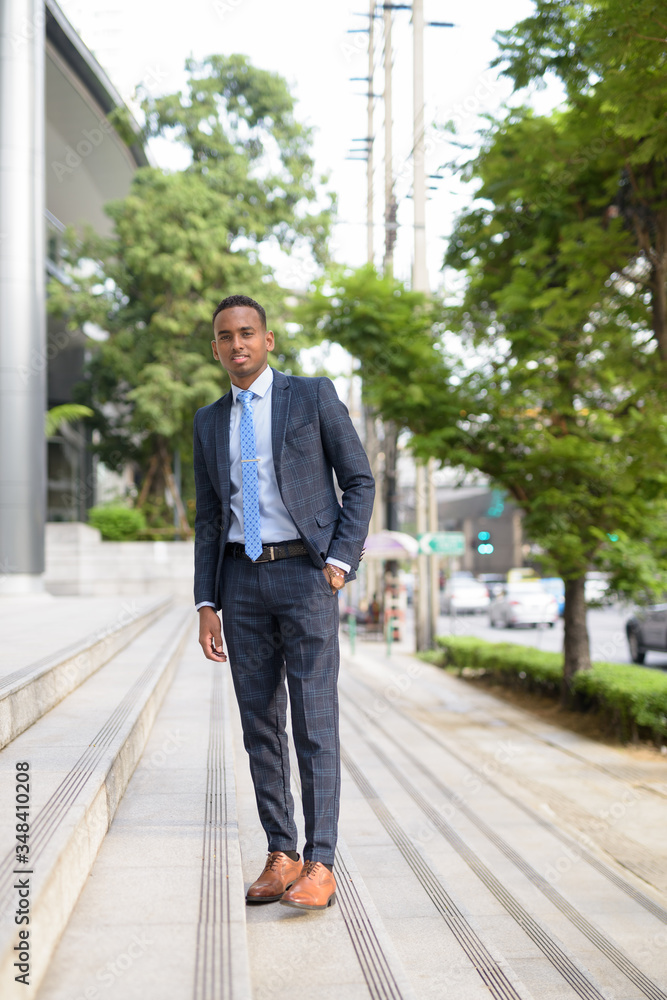 Full body shot of happy young African businessman smiling in the city streets outdoors Full body shot of happy young African businessman smiling in the city streets outdoors