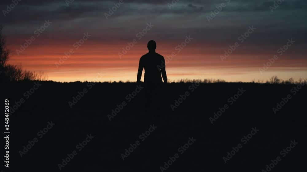 Canada - A man walking in the dark landscape towards the sunset - Wide shot Canada - A man walking in the dark landscape towards the sunset - Wide shot