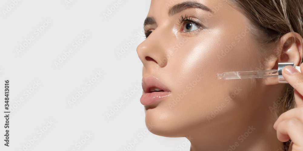Close up of beautiful young woman with essential oil pouring on white background. Concept of cosmetics, makeup, natural and eco treatment, skin care. Shiny and healthy skin, fashion, healthcare.