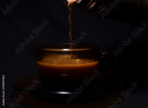 Hot infused tea/coffee being poured in a transparent glass cup and soccer kept in black copy space background. Indian beverages and food photography.