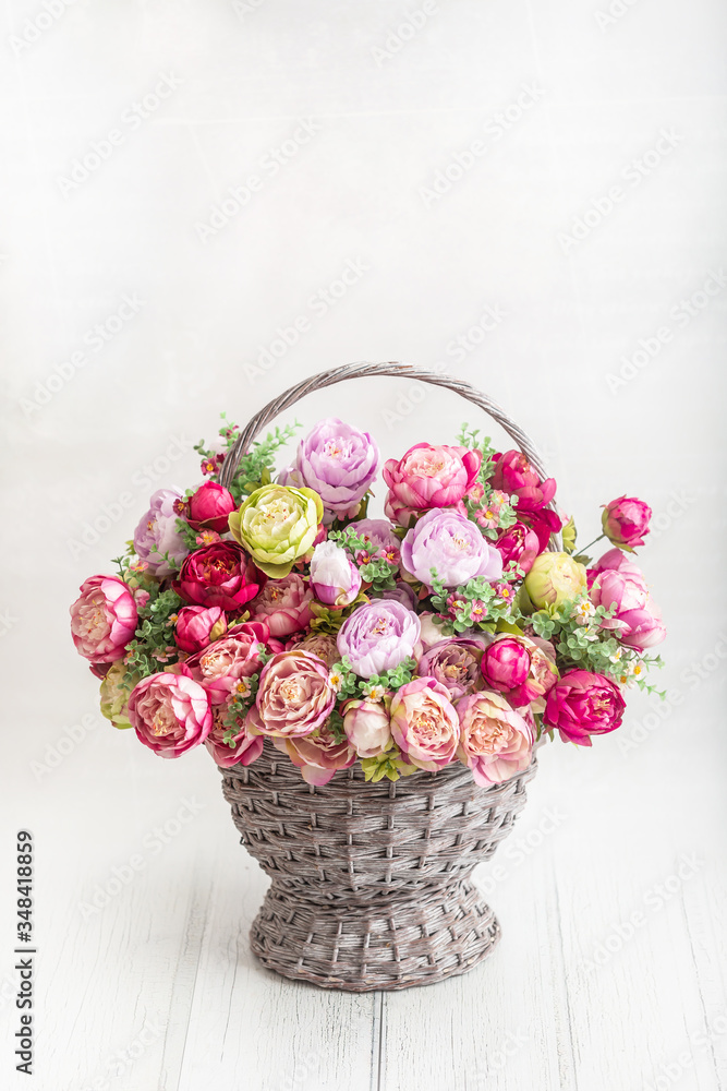 Beautiful bouquet of peonies in an antique basket on a wooden floor