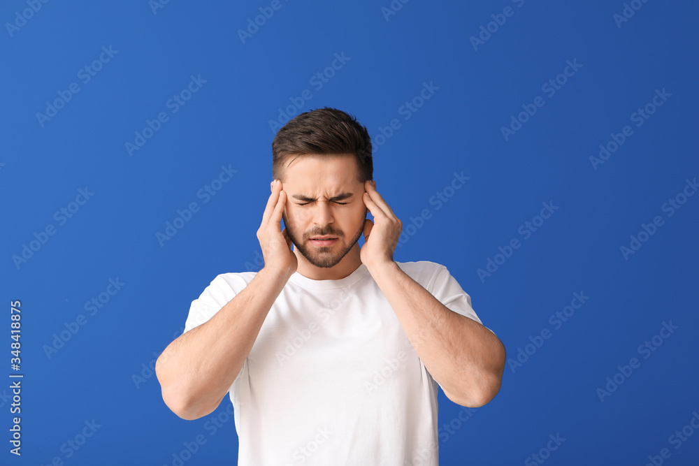 Young man suffering from loud noise on color background Young man suffering from loud noise on color background