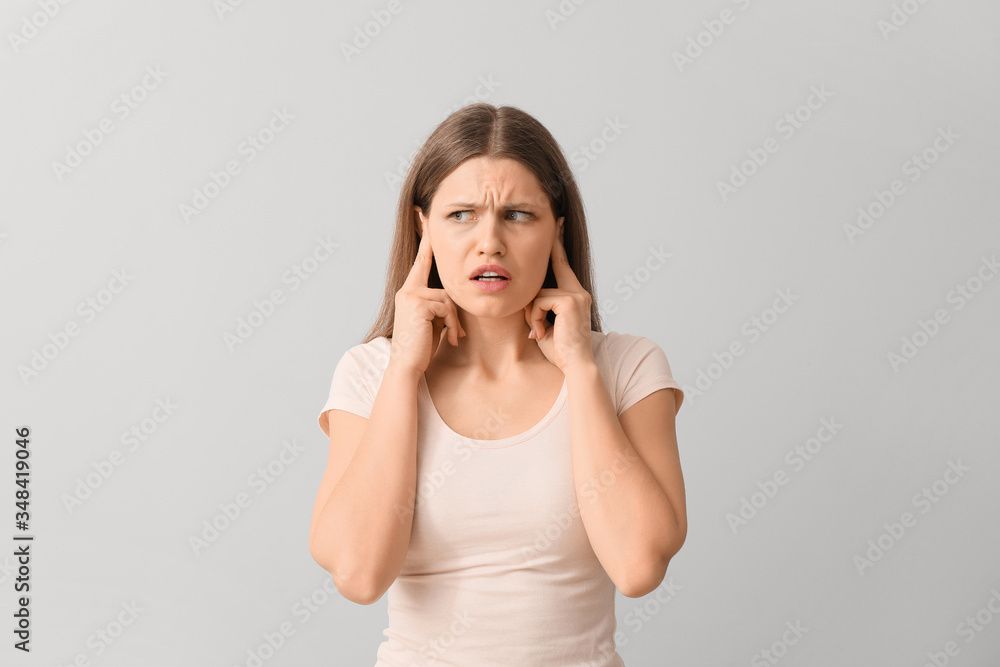 Young woman suffering from loud noise on light background Young woman suffering from loud noise on light background