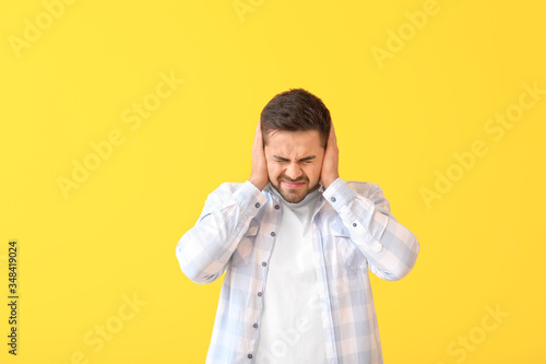 Young man suffering from loud noise on color background photo