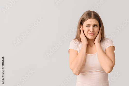 Young woman suffering from loud noise on light background photo