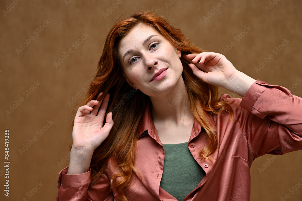Photo taken in the studio on a beige background. Close-up portrait of an actress Caucasian woman with long red hair showing happy emotions. The model is wearing a red shirt. Photo taken in the studio on a beige background. Close-up portrait of an actress Caucasian woman with long red hair showing happy emotions. The model is wearing a red shirt.