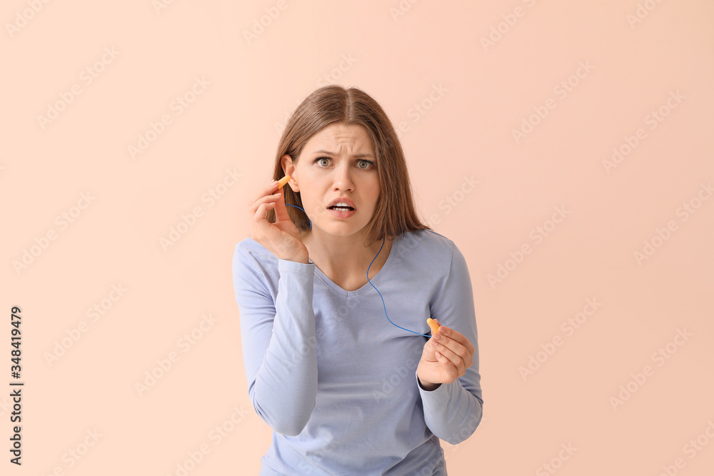 Young woman with ear plugs suffering from loud noise on color background Young woman with ear plugs suffering from loud noise on color background
