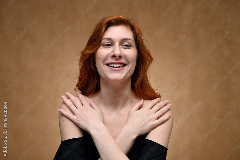 Fototapeta premium Studio large photo portrait of Caucasian young actress woman with long red hair on a beige background. Model poses with a smile and grimace.