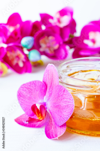 depilation and beauty concept - sugar paste or wax honey for hair removing with wooden waxing spatula sticks in jar on flower background. vertical
