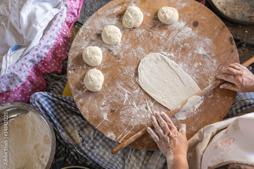 Woman in a black chef's apron roll out the dough for preparing Turkish pancake. 
Woman rolls out dough, close-up. Making Turkish traditional flat cakes.