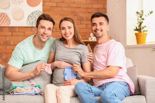 Gay couple and pregnant woman with baby clothes at home © Pixel-Shot