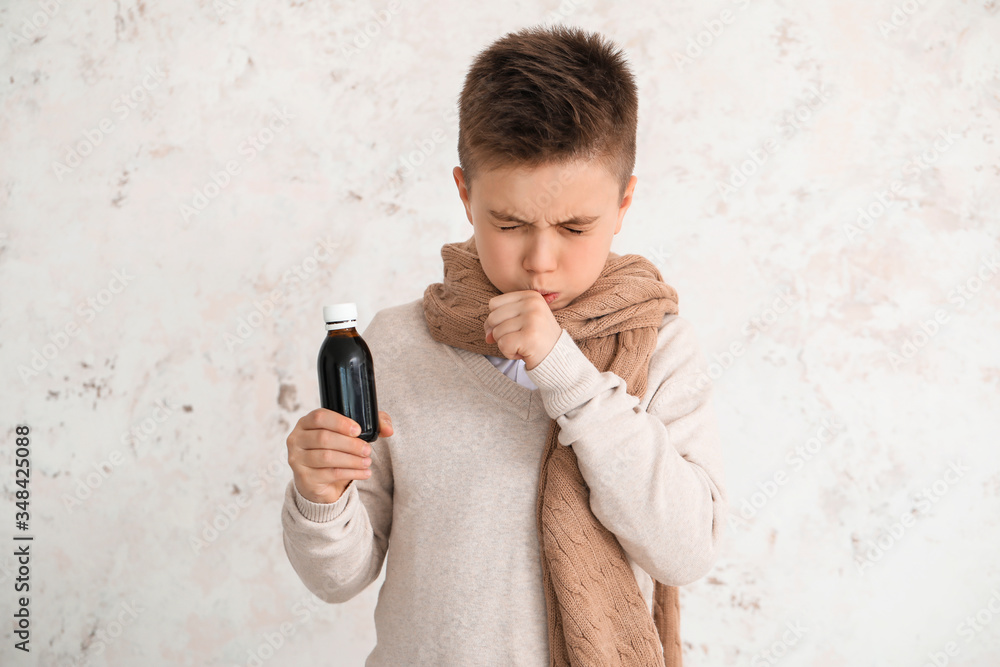 Ill little boy with cough syrup in bottle on light background