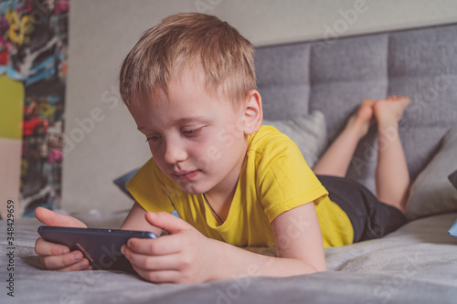Distance education, learning. Boy is lying on the bed with a smartphone in the room. Child with a gadget. Teenage child using smartphone.