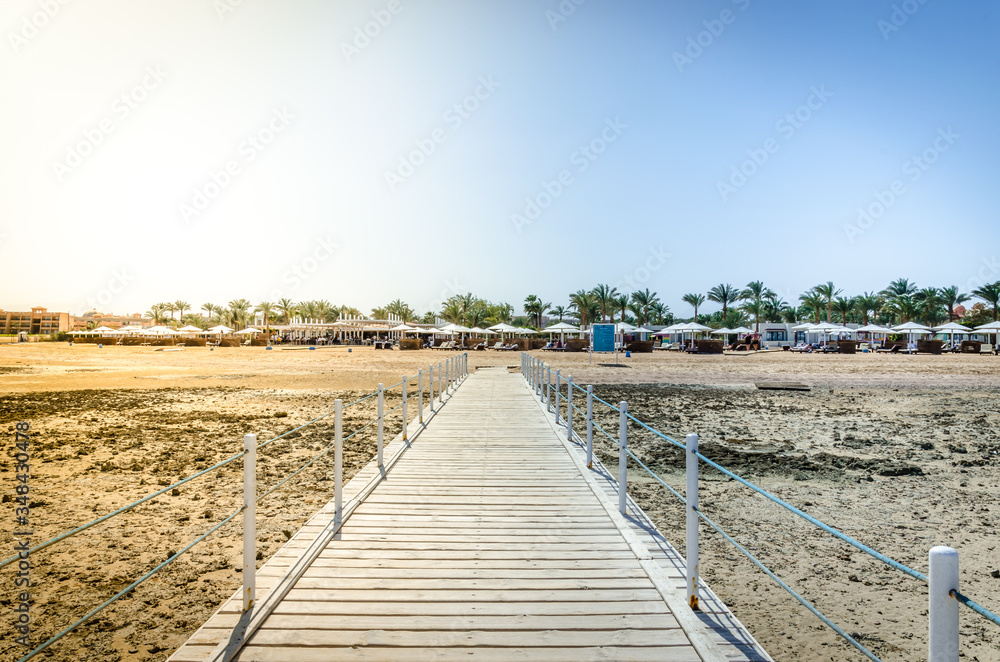 Fototapeta premium Wooden pier leading to the shore on a sunny day/beautiful wooden pier at the sea leading to the shore with blue sky