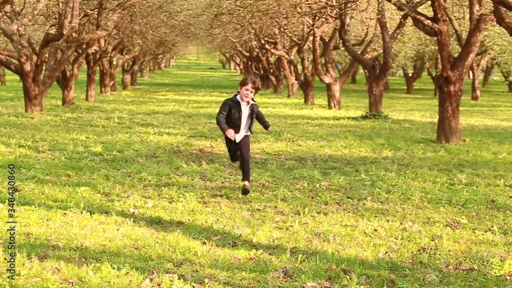Little fashionable boy happily runs through the apple orchard