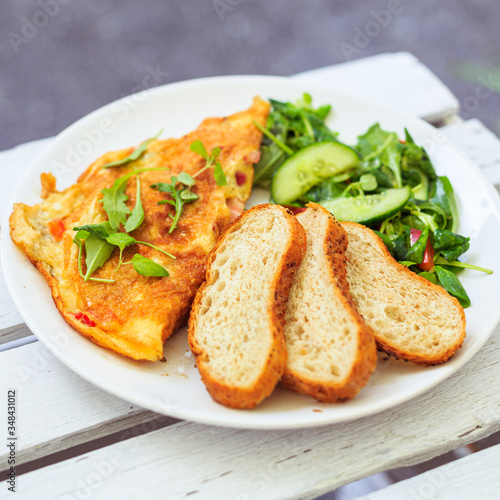 Smażone jajka, omlet, potrawa na śniadanie, biały talerz, dodatki sałatka i warzywa oraz pieczywo.