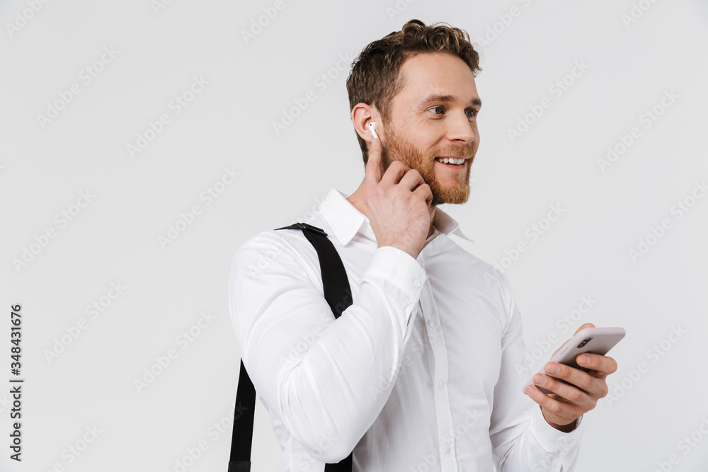 Image of smiling blonde man using cellphone and wireless earphones Image of smiling blonde man using cellphone and wireless earphones
