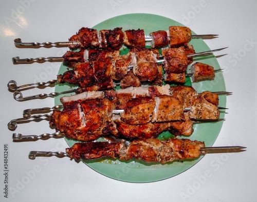 juicy pork skewers on a green dish on a white background