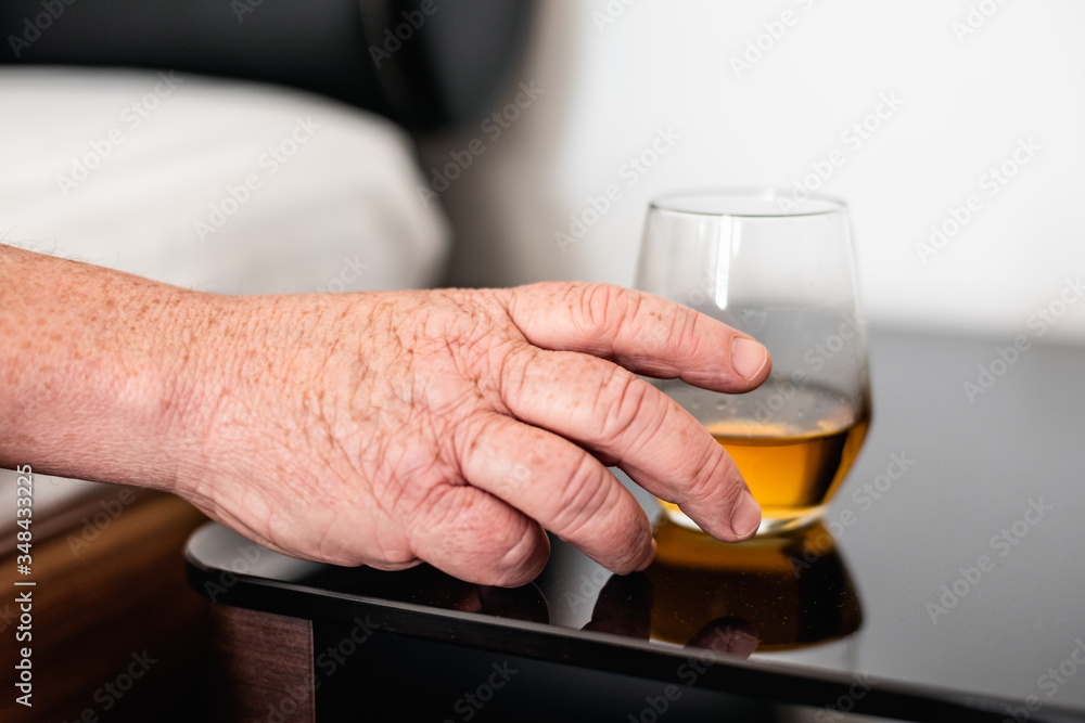 Overweight male hand reaching out from bed for a glass of whisky. Concept of alcoholism, induced by middle-age crisis, loneliness, depression and failure in life. Overweight male hand reaching out from bed for a glass of whisky. Concept of alcoholism, induced by middle-age crisis, loneliness, depression and failure in life.