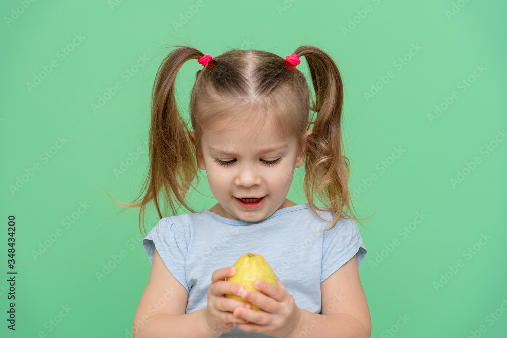 little girl 4 years old in a blue T-shirt on a green background holding a lemon in his hands, looking at it and smiling little girl 4 years old in a blue T-shirt on a green background holding a lemon in his hands, looking at it and smiling
