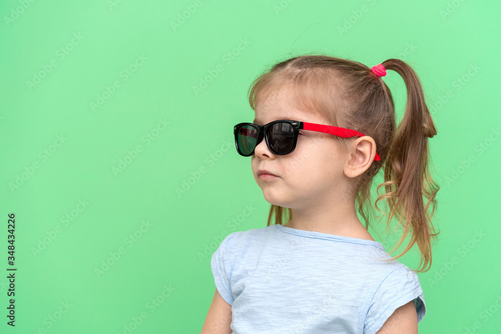 little girl 4 years old in a blue T-shirt on a green background in sunglasses and a blue T-shirt, copy space to the left little girl 4 years old in a blue T-shirt on a green background in sunglasses and a blue T-shirt, copy space to the left