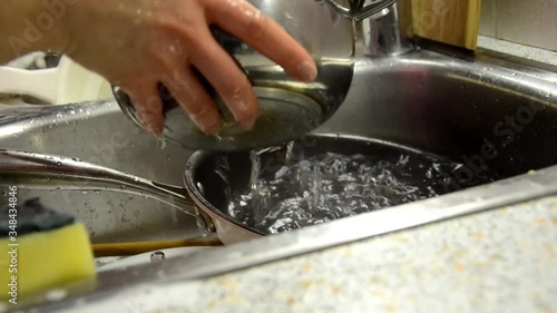 Woman hands rinse plate at the kitchen sink - doing the chores at home with sponge dish detergent. Dish washing routine, static camera. photo