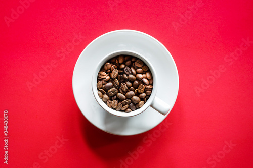Flat lay of roasted coffee beans in white coffee cup with red background 