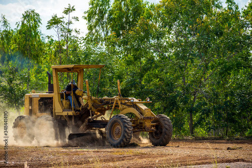 Motor grader clearing and leveling construction site surface with forest in the background. Grader industrial machine on road construction work. photo