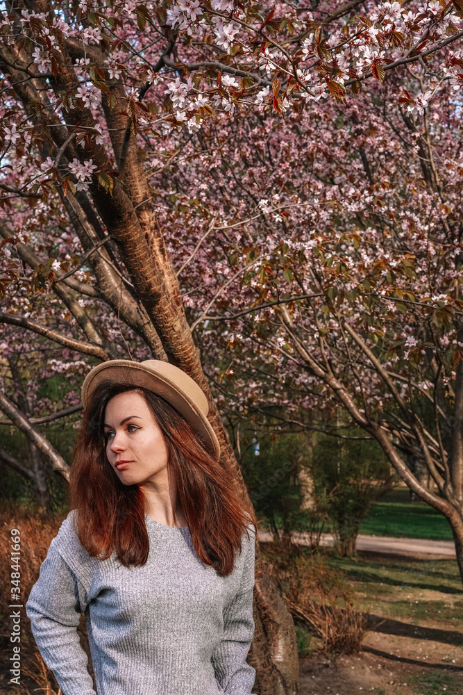 A girl with long hair in a wide-brimmed hat walks in a blooming garden, spring blooming pink cherry trees A girl with long hair in a wide-brimmed hat walks in a blooming garden, spring blooming pink cherry trees