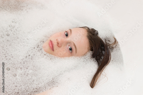 Fotografie Baby girl face in bathtub among soap suds and bubbles