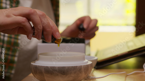 Woman adds essential oil into diffuser in kitchen