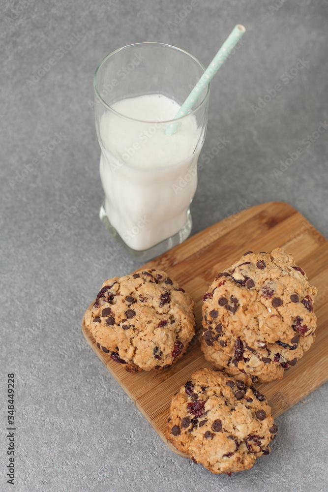 Fresh organic homemade cookies with chocolate chips and dried berries on wooden board with glass of milk on table Fresh organic homemade cookies with chocolate chips and dried berries on wooden board with glass of milk on table