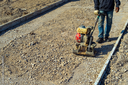 Worker is compacting soil by vibratory plate compactor. Construction equipment. Smooth compaction tool.