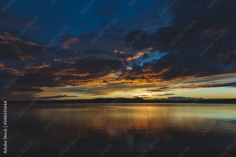 Obraz premium Cloudy yellow orange sunset on Yellowstone lake in national park as natural background wallpaper for computer from travel concept and horizon view of sun and lake which located in United States 