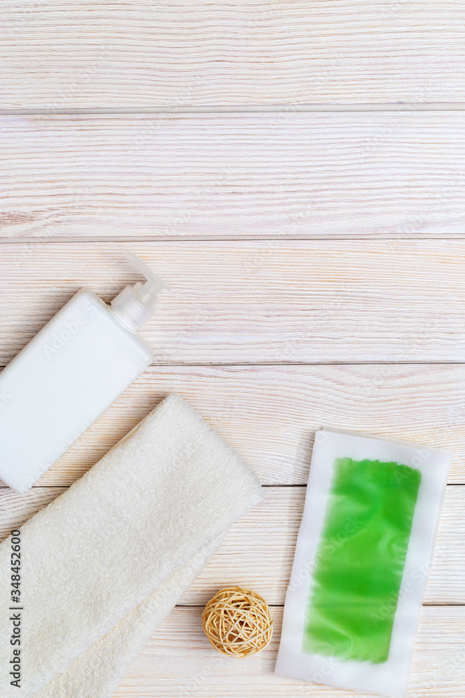 Green waxing strips with mint and cooling effect, body moisturizer and white cotton towel on wooden background with copy space. Flat lay.