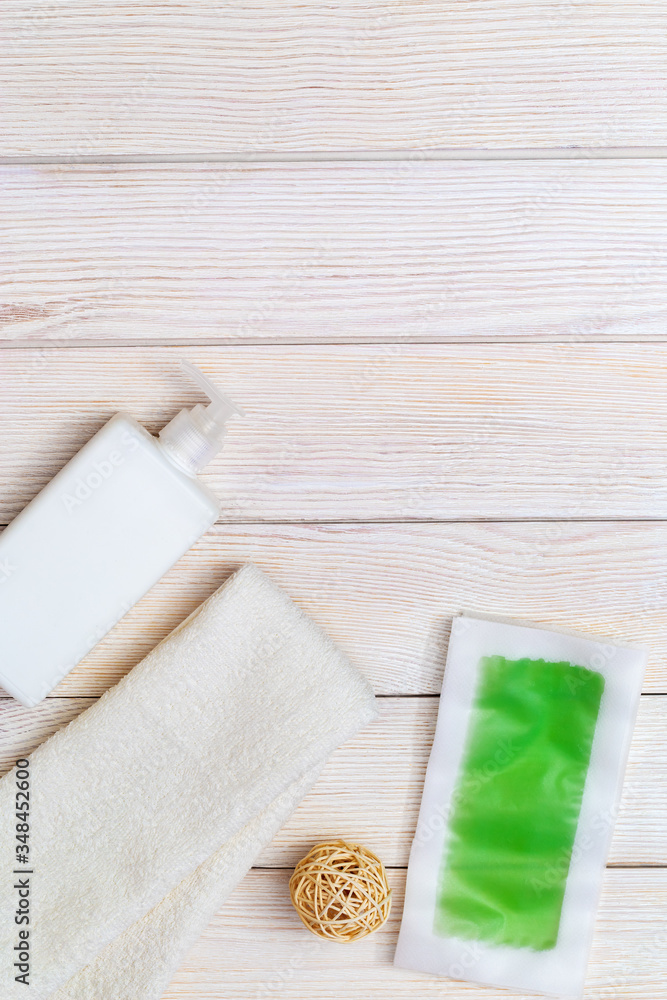 Fototapeta premium Green waxing strips with mint and cooling effect, body moisturizer and white cotton towel on wooden background with copy space. Flat lay.