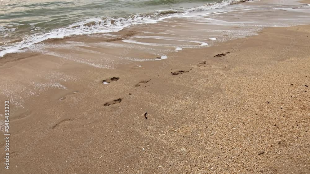 Water wave from the ocean is removing the footstep in the sand on tropical beach. Concept of romantic vacation near sea. Water wave from the ocean is removing the footstep in the sand on tropical beach. Concept of romantic vacation near sea.